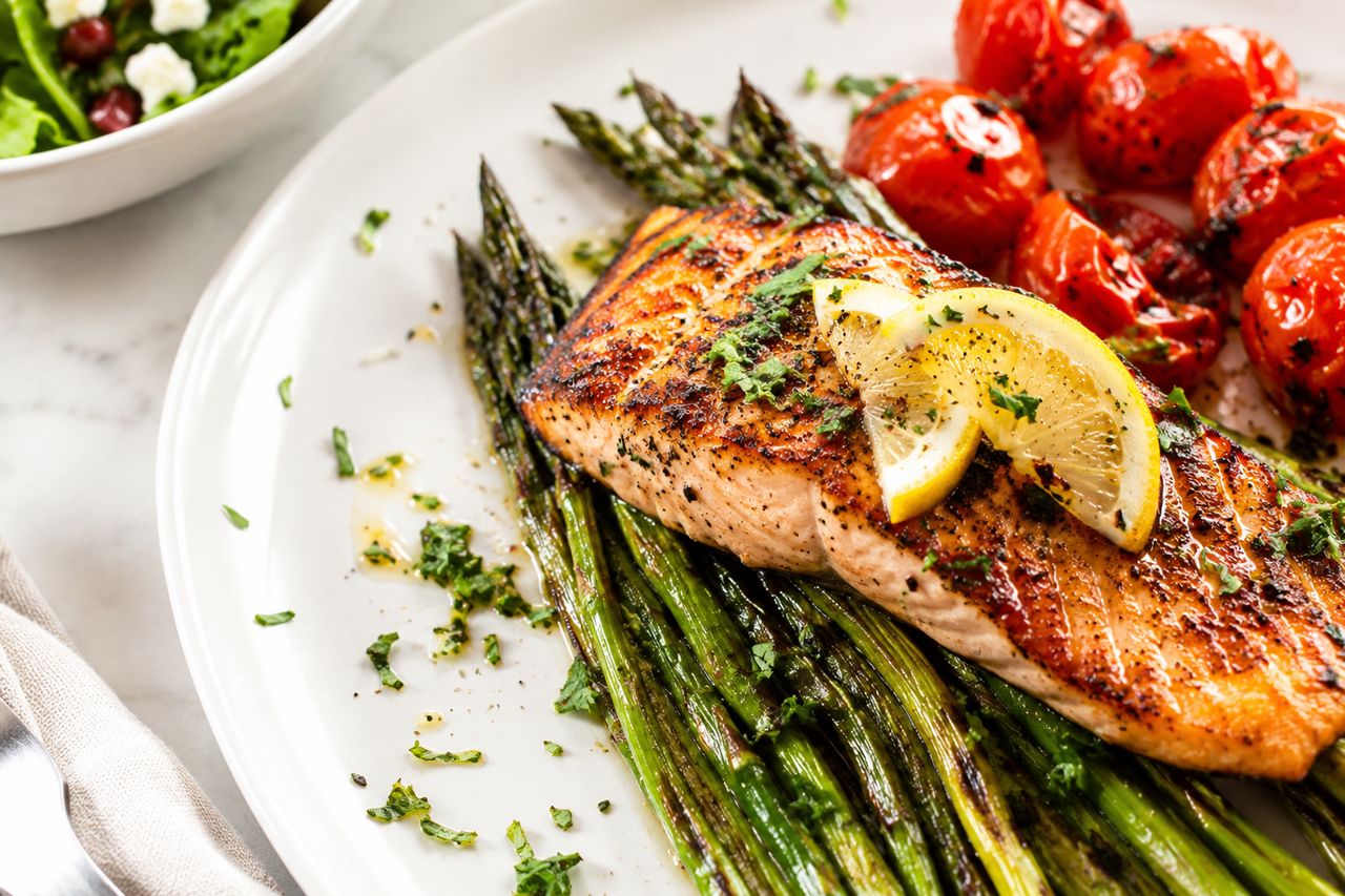 Grilled salmon with lemon on charred asparagus, with roasted tomatoes